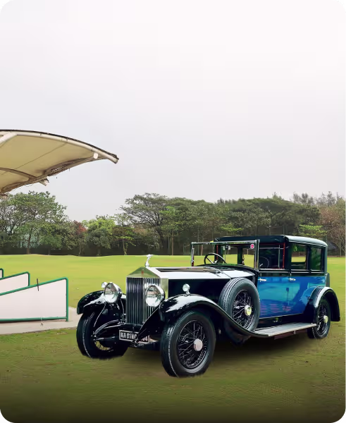 A vintage black and blue Rolls-Royce parked on a grassy field